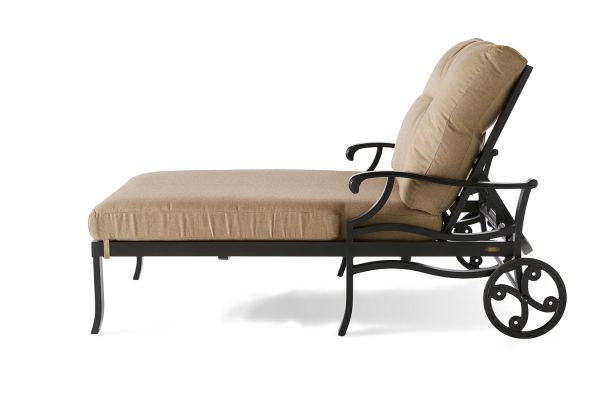 The Anthem Chaise Lounge and a Half features a side view with a beige fabric seat and backrest. It has a dark metal frame, ornate armrests, and two large rear wheels for easy mobility.