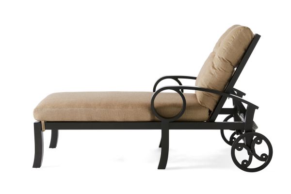 Side view of the Eclipse Chaise Lounge, a cushioned beige chair with a black metal frame, featuring decorative circular armrests and two rear wheels for easy movement.