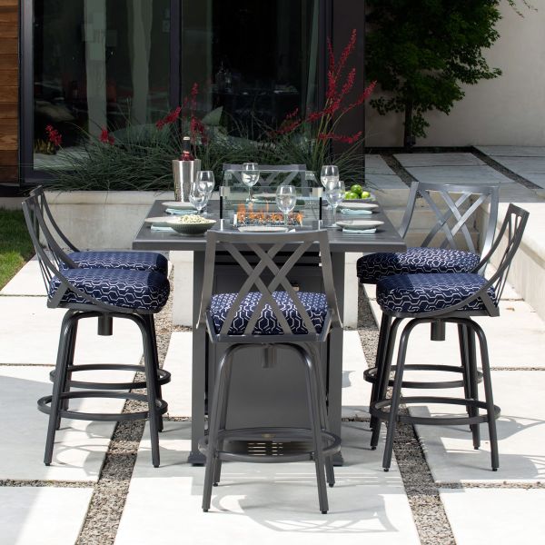 Outdoor dining set with a square glass-top table and built-in fire pit, surrounded by four chairs. The scene features glasses, a salad, and a lush garden backdrop. Paired perfectly with the M Series Armless Bar Stool to complete the experience.