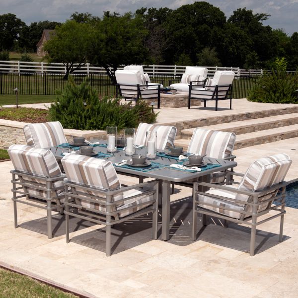 A patio features a rectangular table with plates and glasses, surrounded by eight striped cushioned chairs. In the back, there are two Sarasota Cushion RAF Sectional End Units near a pool, set against a backdrop of grass, trees, and fencing.