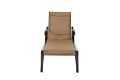 The Volare Sling Adjustable Chaise Lounge sits on a wooden deck by the lake, surrounded by trees that provide shade. Nearby, a round table with red napkins, plates, and wine glasses complements the scene, while a wicker basket centerpiece adds rustic char