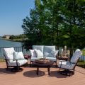 An outdoor patio features an Albany Dining Armchair set with light blue cushions around a round table. In the background, a lake and lush greenery under a clear blue sky create a serene and inviting scene.